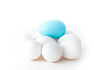 A close up photograph of a pile of real chicken eggs and a light blue plastic Easter egg on top isolated on a white background making a beautiful holiday wallpaper with white open space around image.
