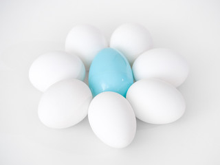 Photograph of a cute flower shape created from the arrangement of white chicken eggs as petals and a blue plastic Easter egg at the center making a great holiday background image.