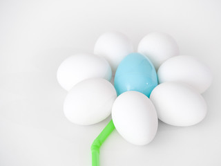 Photograph of a cute flower shape created from the arrangement of white chicken eggs as petals and a blue plastic Easter egg and green flexible straw making a great holiday background image or craft.