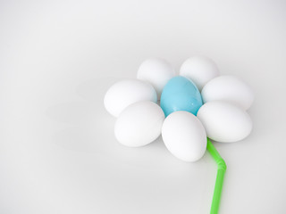 Photograph of a cute flower shape created from the arrangement of white chicken eggs as petals and a blue plastic Easter egg and green flexible straw making a great holiday background image or craft.