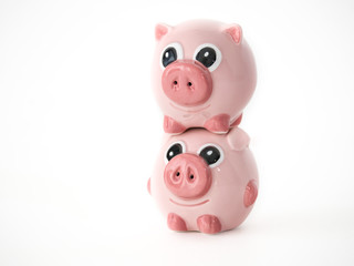 Funny close up photograph of two pink round pig ceramic salt and pepper shakers piggy backing or stacked on one another isolated on a white background with space around the animal shaped objects.