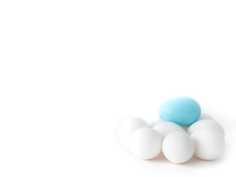 A close up photograph of a pile of real chicken eggs and a light blue plastic Easter egg on top isolated on a white background making a beautiful holiday wallpaper with white open space around image.