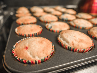 Close up view of freshly made cupcakes in red and green wax wrappers sitting in a metal cupcake pan on top of the stove in the kitchen.