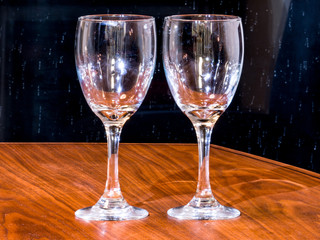 Two empty wine glasses set on a black walnut table top with dark background for a romantic backdrop or wallpaper image.