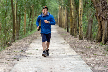 Asian runner in sport suit are running with happiness action drinking the water from sport bottle with relax action in deep forest in evening time, lifestyle and leisure concept