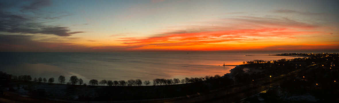 Beautiful wide panorama landscape photograph of a vivid red orange and yellow sunrise in Chicago over the water of Lake Michigan