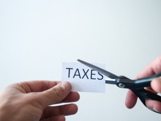Closeup photograph of man holding black handle scissors and cutting a paper with the word taxes on...