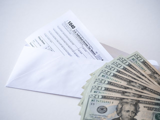 Close up photograph of 1040 federal department of treasury individual income tax return form with a pile of 20 dollar bills and a mailing envelope representing tax deduction savings.