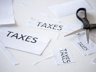 Close up of black handle scissors and printed paper with the word taxes on it cut in half...