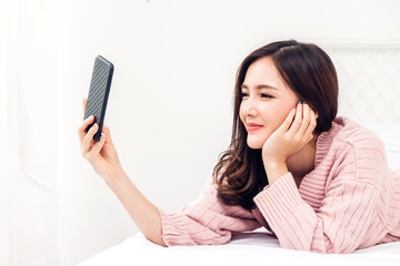 Fototapeta premium Happy woman relaxing using and talking technology of smartphone and checking social apps on the bed at home.technology and communication concept