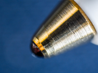 An extreme closeup macro detail microscopic image of the tip of a ballpoint pen with machined gold...