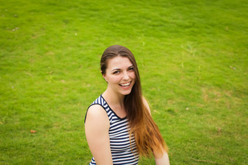 Naklejka na ściany i meble Beautiful happy brunette young woman smiling on green grass outside