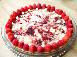 Closeup photograph of a beautiful and colorful vibrant whole white chocolate raspberry cheesecake dessert with fruit topping on a wood butcher block background for a mouthwatering birthday treat.