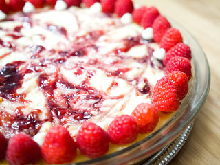 Closeup photograph of a beautiful and colorful vibrant whole white chocolate raspberry cheesecake dessert with fruit topping on a wood butcher block background for a mouthwatering birthday treat.