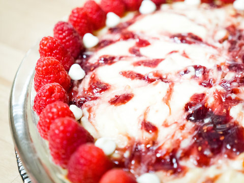 Closeup photograph of a beautiful and colorful vibrant whole white chocolate raspberry cheesecake dessert with fruit topping on a wood butcher block background for a mouthwatering birthday treat.