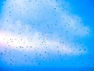 Blue water droplets on the glass of a window during a rain storm at sunset