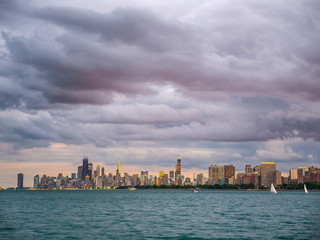 Gorgeous landscape panoramic photograph of the beautiful Chicago skyline with buildings at horizon and Lake Michigan in foreground and pink, orange, and purple fluffy clouds in sky above.