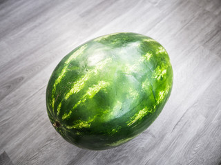 Closeup of a green and yellow striped whole watermelon on a gray wood grain background.