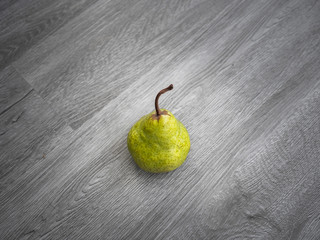 A single ripe yellow pear and stem on a gray wood grain background.