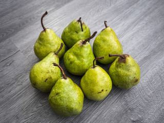 A group of ripe yellow pears with stems on a gray wood grain background.