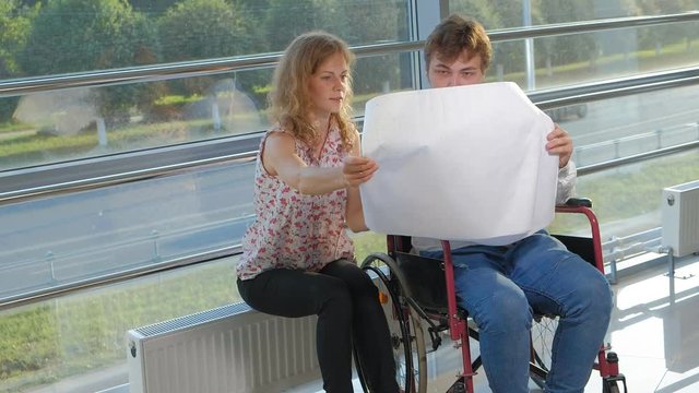 disabled businessman on a wheelchair in a window with a picture on a large sheet of paper discussing work with a business woman, discussion in the office...