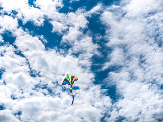 Soaring colorful striped kite with red, orange, yellow, green, purple and blue colors on beautiful spring day in Chicago with blue sky and white cumulus clouds above.