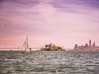 San Francisco Skyline Sunset  with sailboat on the water passing Alcatraz Island, a helicopter...