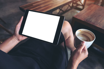 Mockup image of woman's hands holding black tablet pc with blank white desktop screen while sitting and drinking coffee in cafe