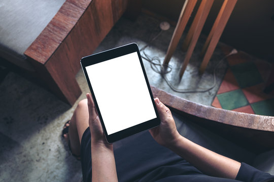 Top view mockup image of a woman sitting and holding black tablet pc with blank white desktop screen