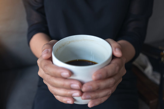 Closeup image of a woman's hands holding a white cup of hot coffee