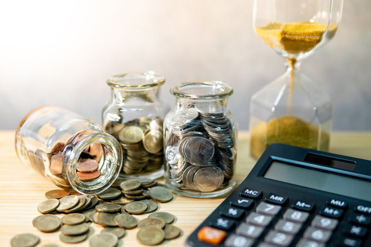 Calculator with coin in currency glass jar and hourglass on wooden table. Compound interest rate calculation. Financial business plan. Time investment concept
