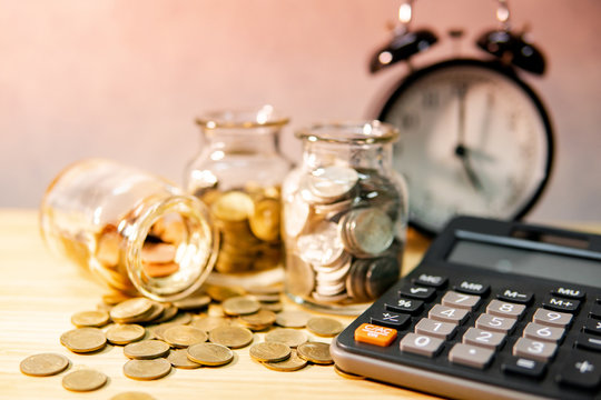 Calculator with coin in currency glass jar and clock on wooden table. Compound interest rate calculation. Financial business plan. Time investment concept