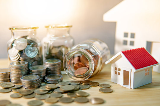 House models with coin in currency glass jars and spilling on wooden table. Saving money for future retirement. Home mortgage loan rate. Real estate development or property investment concept