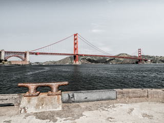 A beautiful landscape view of the famous Golden Gate Bridge travel destination in San Francisco with hills beyond and water and rusted metal boat dock cleat in foreground on a pier.