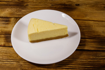Piece of tasty sweet New York cheesecake in a white plate on wooden table