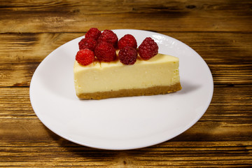 Piece of tasty New York cheesecake with raspberries in a white plate on wooden table