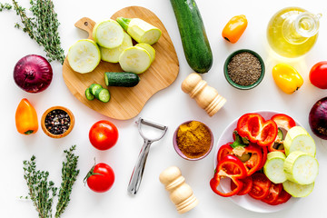 Cooking vegetable stew concept. Fresh vegetables squash, bell pepper, tomato, spices and cutting doard on white background top view