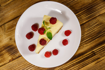 Piece of tasty New York cheesecake with raspberries in a white plate on wooden table. Top view