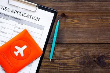 Fill visa application form. Empty blank near passport cover with airplane on dark wooden background...