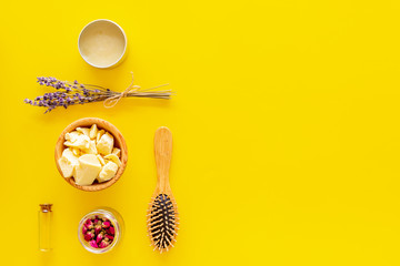 Hair treatment with natural products. Jojoba, argan, coconut oil near bunch of lavender and hairbrush on yellow background top view copy space