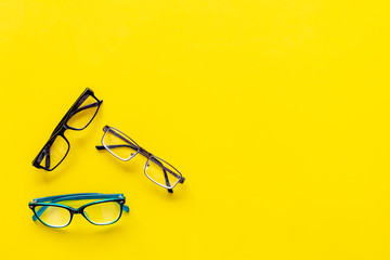 Glasses with transparent optical lenses on yellow background top view copy space