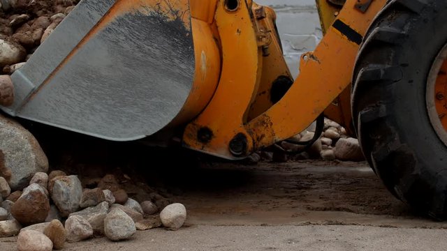 A large yellow loader collects crushed stone in a bucket, close-up, stones and tractor