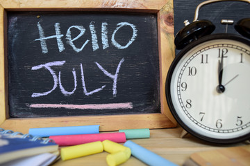 Hello july. Back to school concept. Alarm clock on wooden with blackboard on background