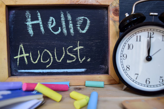 Hello august. Back to school concept. Alarm clock on wooden with blackboard on background