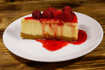 Piece of tasty New York cheesecake with raspberries and raspberry jam in a white plate on wooden table