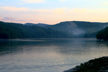 The cute still lake water at sunset with green hills in distance. Natural landscape photo
