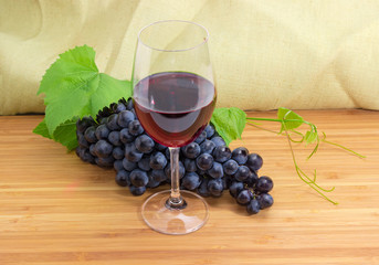 Glass of red wine against of blue grapes cluster