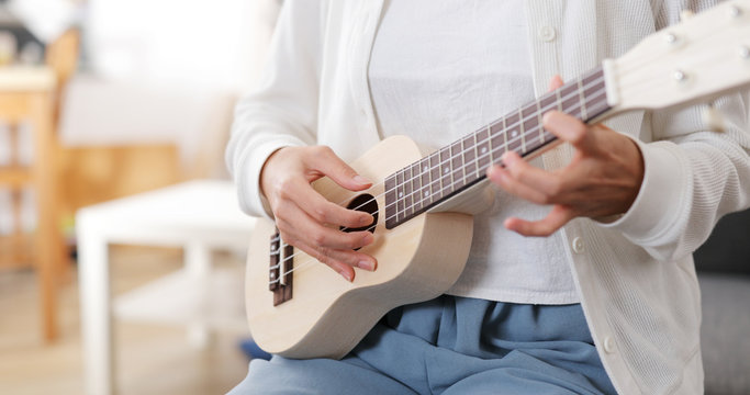 Woman play a song on ukulele at home