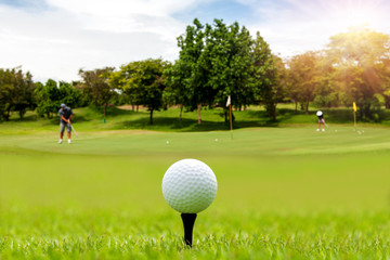 White Golf ball on tee ready to be shot on blurred beautiful landscape of golf course in bright day time with golfer playing golf on course. Sport, Recreation, Relax in holiday concept.	