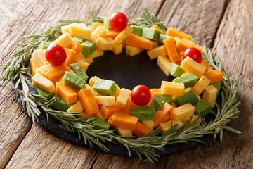 Assorted pesto cheese, cheddar, Mimolette with tomatoes and rosemary in the form of a wreath close-up. horizontal